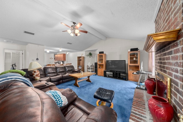 carpeted living room featuring a brick fireplace, a textured ceiling, lofted ceiling with beams, and ceiling fan