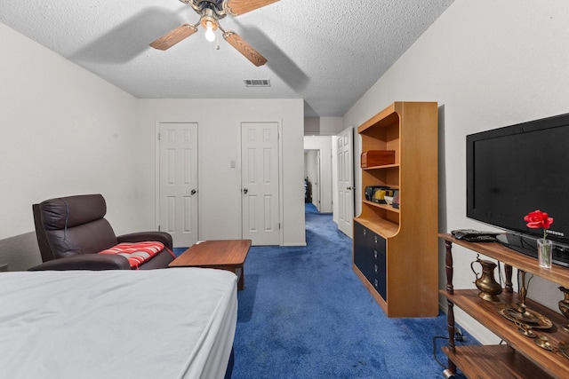 bedroom featuring a textured ceiling, ceiling fan, two closets, and dark carpet