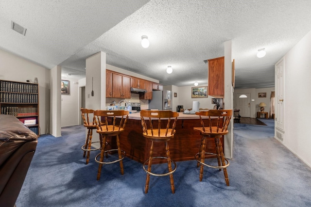 kitchen featuring a breakfast bar, kitchen peninsula, appliances with stainless steel finishes, and dark carpet