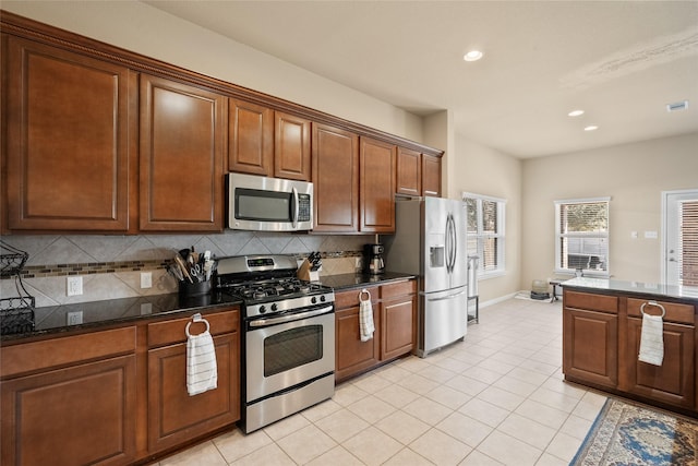 kitchen with appliances with stainless steel finishes, light tile patterned floors, backsplash, and dark stone counters