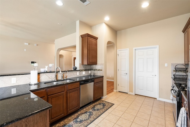 kitchen featuring sink, backsplash, dark stone counters, light tile patterned floors, and stainless steel appliances