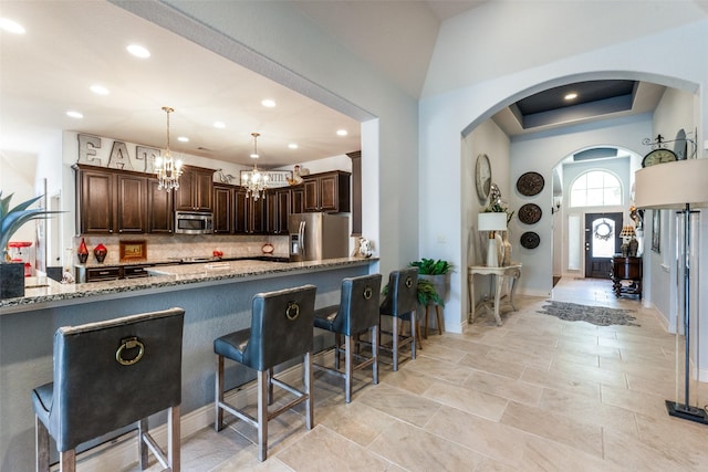 kitchen featuring light stone countertops, appliances with stainless steel finishes, dark brown cabinetry, tasteful backsplash, and hanging light fixtures