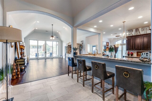 kitchen featuring lofted ceiling, pendant lighting, dark brown cabinetry, a kitchen breakfast bar, and stone countertops