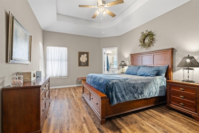 1536 Kings Ranch Rd, Bandera, TX 78003 - bedroom with light wood-style flooring, a tray ceiling, baseboards, ceiling fan, and connected bathroom
