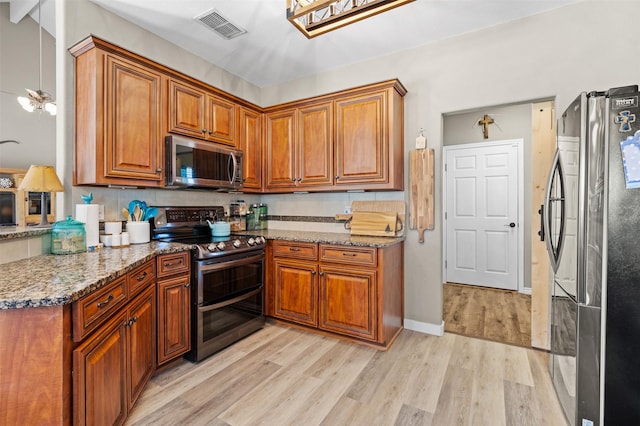 kitchen with a skylight, appliances with stainless steel finishes, light stone countertops, and light hardwood / wood-style flooring