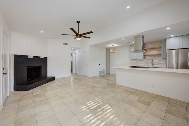 unfurnished living room with a brick fireplace, light tile patterned floors, lofted ceiling, and ceiling fan