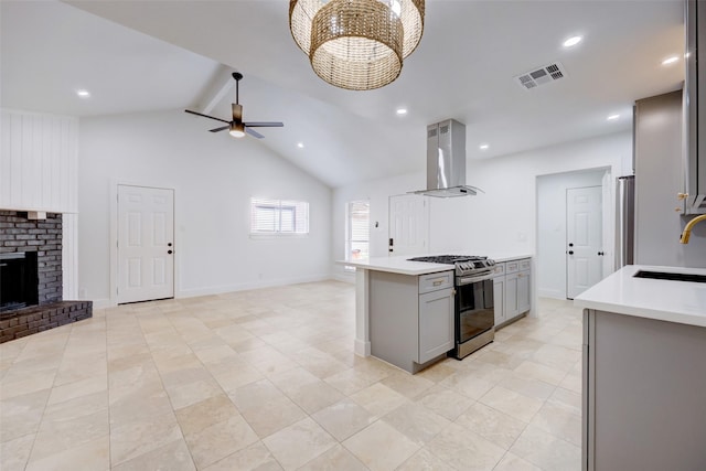 kitchen with stainless steel gas range oven, island exhaust hood, gray cabinetry, lofted ceiling, and a fireplace