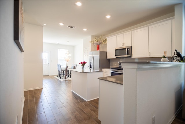 kitchen featuring appliances with stainless steel finishes, a center island, white cabinetry, decorative backsplash, and hanging light fixtures