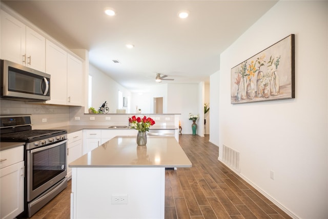 kitchen featuring tasteful backsplash, visible vents, appliances with stainless steel finishes, a peninsula, and dark wood-style floors