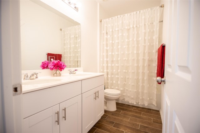 bathroom featuring wood tiled floor, toilet, double vanity, and a sink