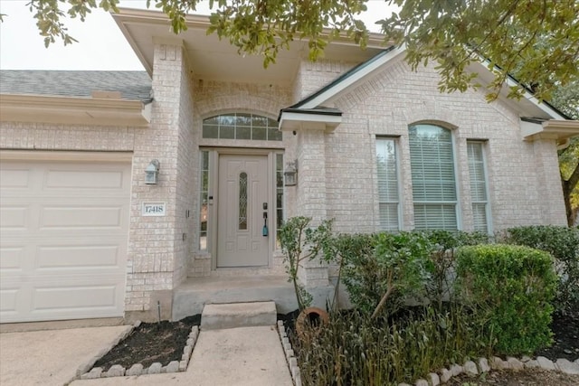 view of exterior entry featuring a garage and brick siding