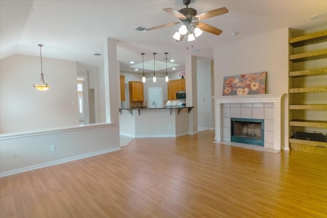 unfurnished living room with ceiling fan, vaulted ceiling, a tile fireplace, and light hardwood / wood-style flooring