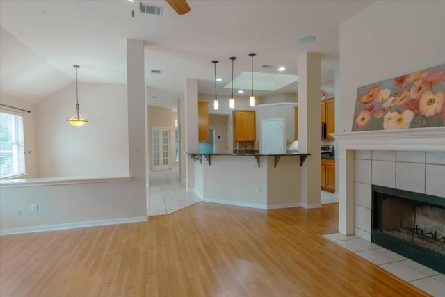 unfurnished living room with a tile fireplace, lofted ceiling, ceiling fan, and light hardwood / wood-style floors