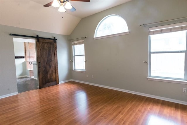 spare room featuring vaulted ceiling, a barn door, dark hardwood / wood-style floors, and ceiling fan