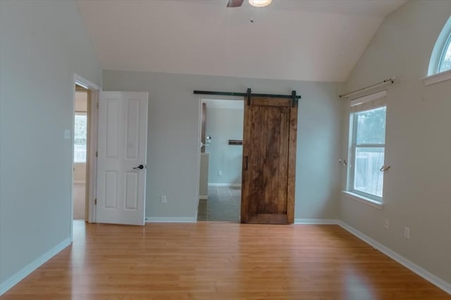 unfurnished bedroom featuring ceiling fan, lofted ceiling, a barn door, and light wood-type flooring