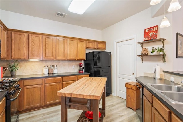 kitchen featuring tasteful backsplash, pendant lighting, black appliances, sink, and light hardwood / wood-style flooring