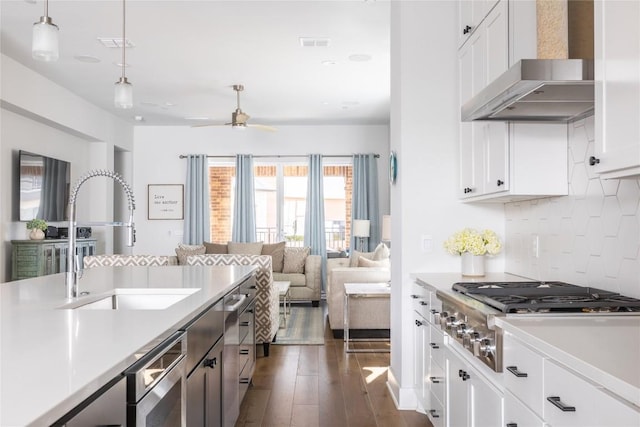 kitchen with stainless steel gas cooktop, light countertops, white cabinets, a sink, and wall chimney exhaust hood