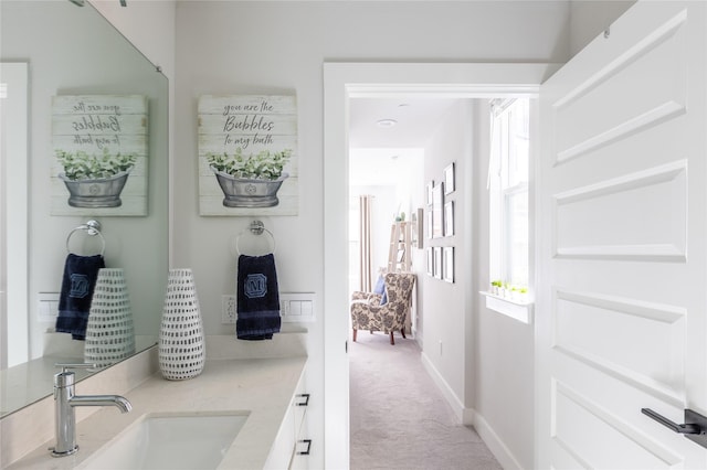 corridor featuring baseboards, a sink, and light colored carpet