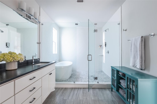 bathroom with a stall shower, a soaking tub, visible vents, and vanity