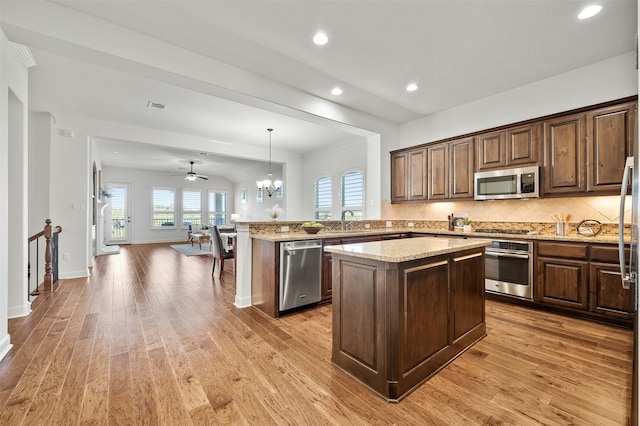 kitchen featuring appliances with stainless steel finishes, a center island, decorative light fixtures, backsplash, and kitchen peninsula