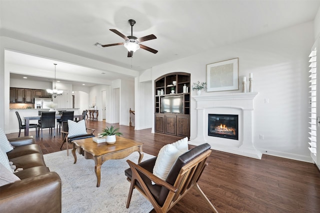 living room with built in features, ceiling fan with notable chandelier, and dark hardwood / wood-style floors