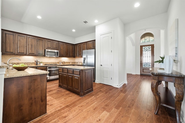 kitchen with light stone countertops, dark brown cabinetry, appliances with stainless steel finishes, and wood-type flooring