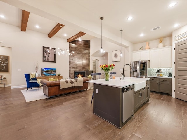 kitchen with sink, white cabinetry, an island with sink, pendant lighting, and beam ceiling