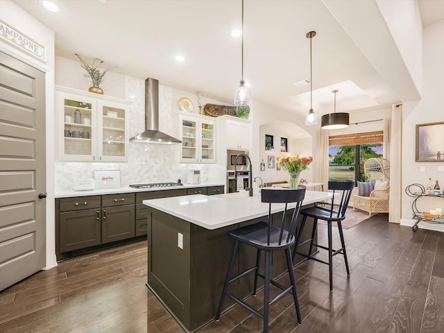 kitchen with pendant lighting, a breakfast bar area, appliances with stainless steel finishes, white cabinets, and wall chimney exhaust hood