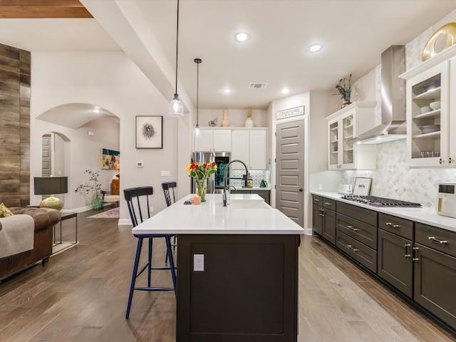 kitchen featuring sink, white cabinets, a kitchen bar, wall chimney range hood, and a center island with sink