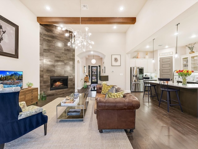 living room with an inviting chandelier, a tile fireplace, dark hardwood / wood-style floors, and beamed ceiling