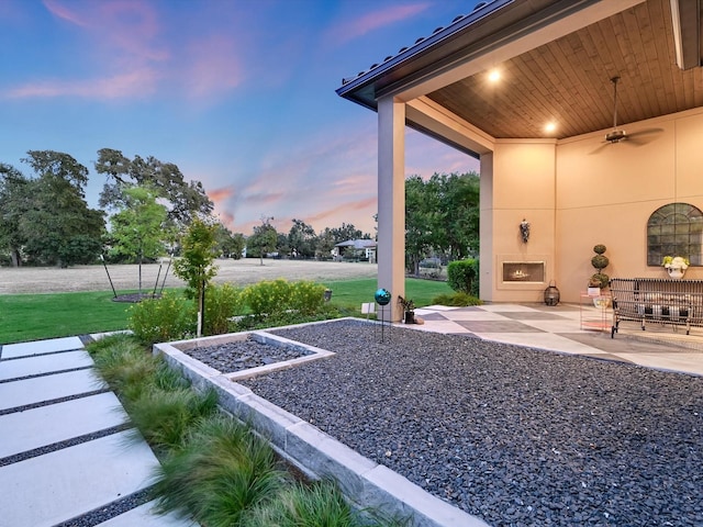 yard at dusk with a patio, ceiling fan, and exterior fireplace