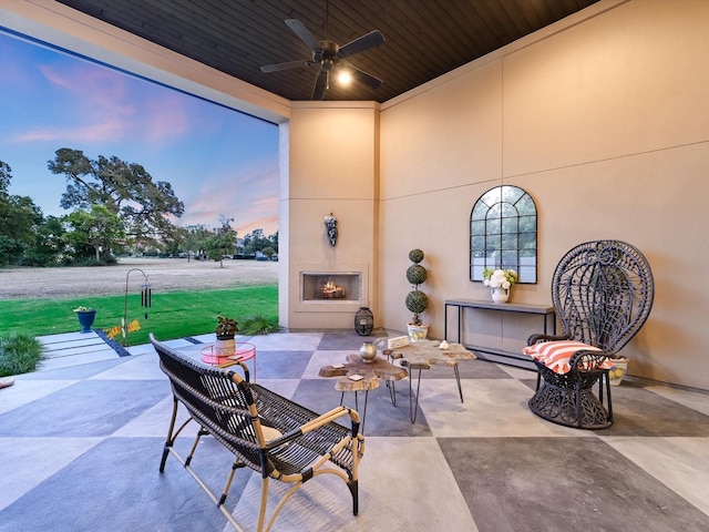 patio terrace at dusk with ceiling fan and an outdoor fireplace