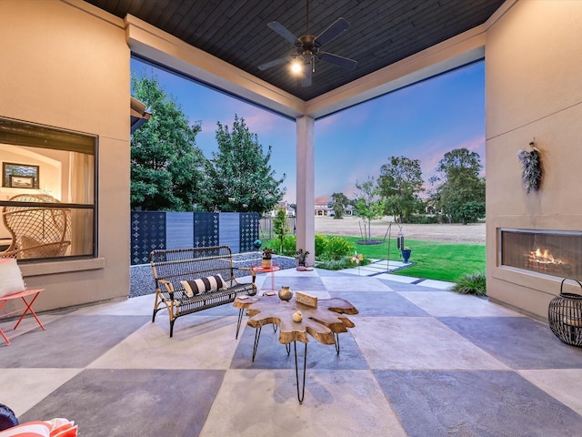 patio terrace at dusk featuring ceiling fan and an outdoor fireplace