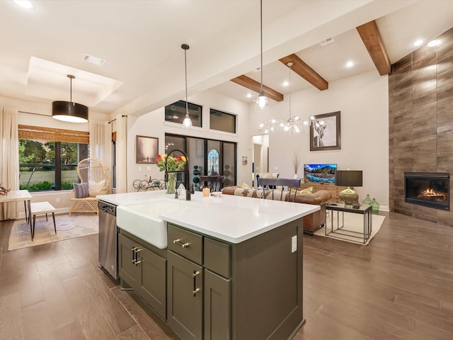 kitchen with hanging light fixtures, a center island with sink, stainless steel dishwasher, dark hardwood / wood-style floors, and a fireplace