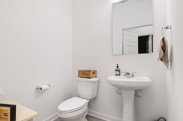 half bathroom featuring toilet, baseboards, and wood finished floors