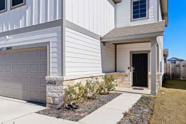 property entrance featuring a garage, a shingled roof, fence, stone siding, and board and batten siding