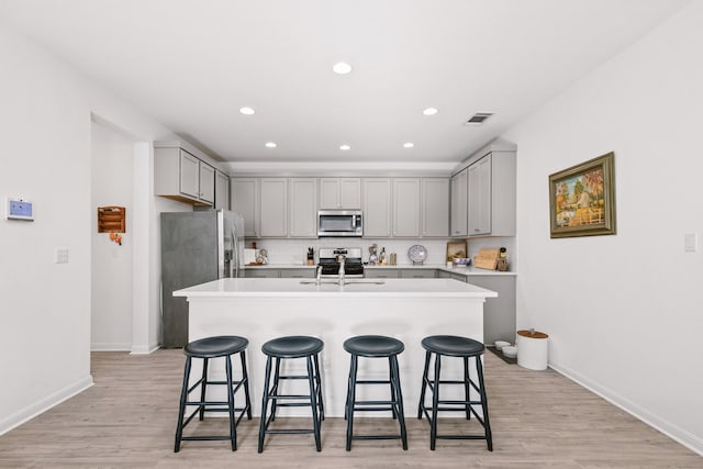 kitchen with a kitchen breakfast bar, appliances with stainless steel finishes, gray cabinetry, and a kitchen island with sink