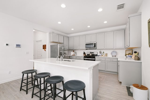 kitchen featuring gray cabinets, appliances with stainless steel finishes, a kitchen breakfast bar, decorative backsplash, and a center island with sink