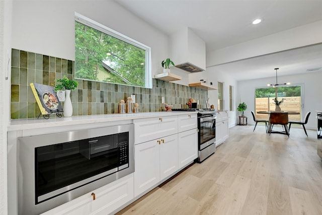 kitchen featuring white cabinetry, stainless steel range with gas cooktop, decorative backsplash, built in microwave, and hanging light fixtures