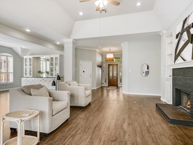 living room featuring lofted ceiling, wood-type flooring, a fireplace, ceiling fan, and crown molding