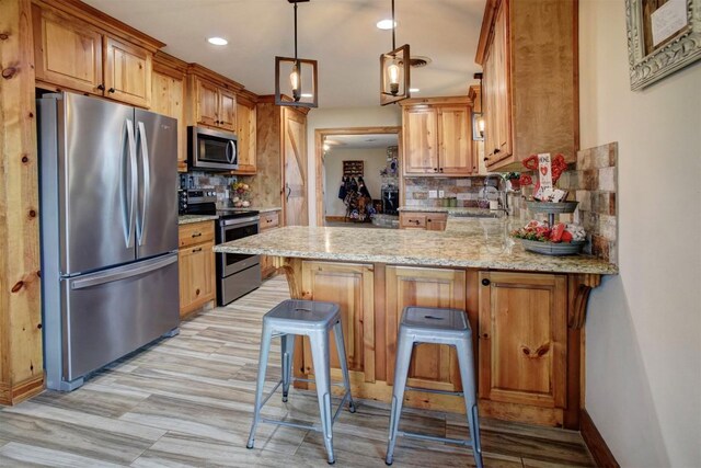 kitchen with backsplash, kitchen peninsula, appliances with stainless steel finishes, and a kitchen breakfast bar