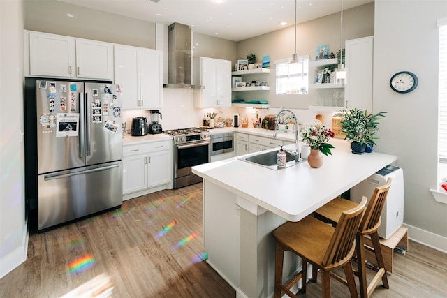 kitchen featuring pendant lighting, appliances with stainless steel finishes, wall chimney range hood, white cabinetry, and kitchen peninsula