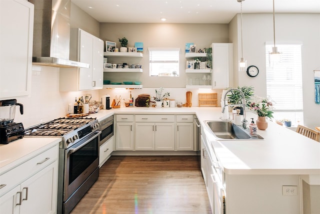 kitchen with decorative light fixtures, gas stove, sink, white cabinetry, and wall chimney exhaust hood