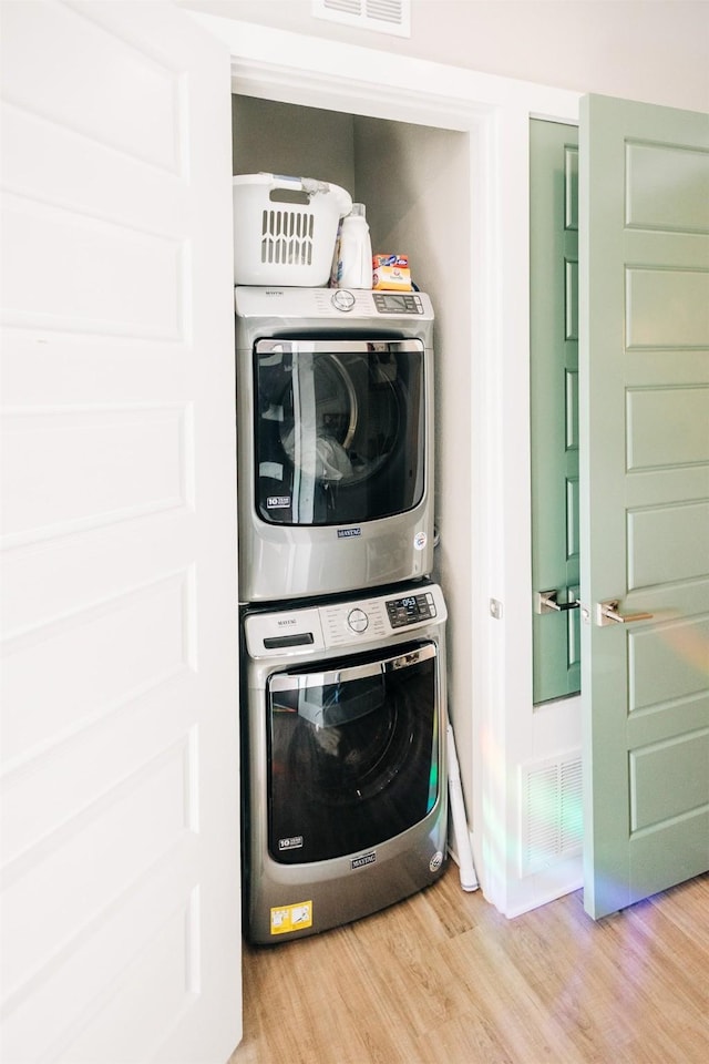 laundry room featuring stacked washer and dryer and wood-type flooring