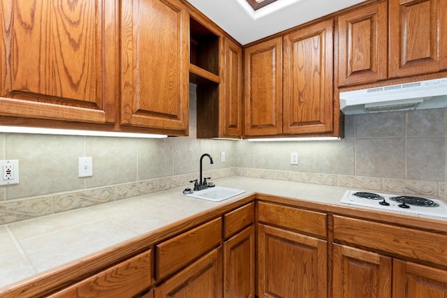 112 Center Cove Iii Loop, Spicewood, TX 78669 - kitchen featuring under cabinet range hood, tile counters, brown cabinetry, and tasteful backsplash