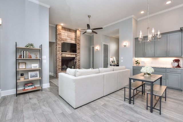 living room with a brick fireplace, crown molding, and ceiling fan with notable chandelier