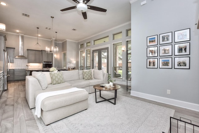 living room with crown molding, light hardwood / wood-style floors, ceiling fan with notable chandelier, and french doors