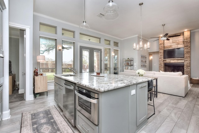 kitchen with appliances with stainless steel finishes, an island with sink, sink, hanging light fixtures, and gray cabinetry