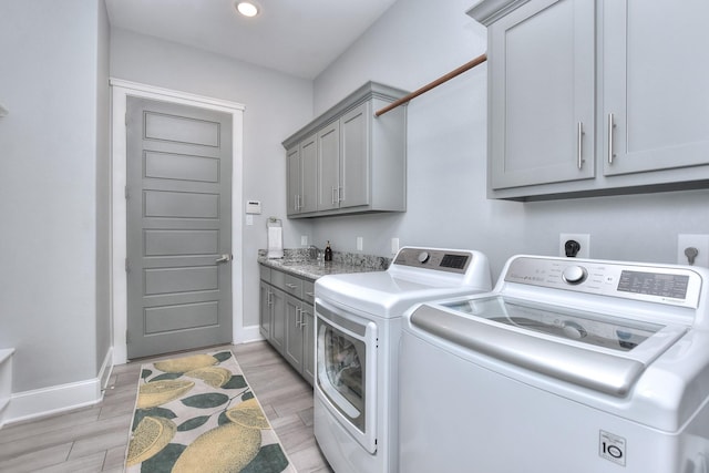 clothes washing area with cabinets, washer and clothes dryer, and light hardwood / wood-style floors