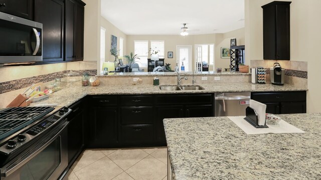 kitchen featuring light stone counters, light tile patterned flooring, dark cabinets, stainless steel appliances, and a sink